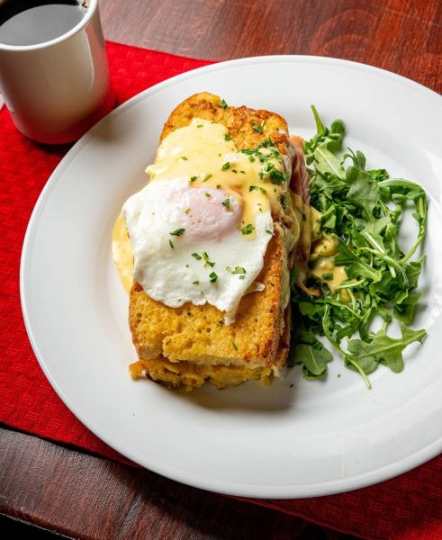 Plate of brunch featuring a slice of bread topped with poached egg and hollandaise sauce, accompanied by fresh arugula and a cup of coffee.