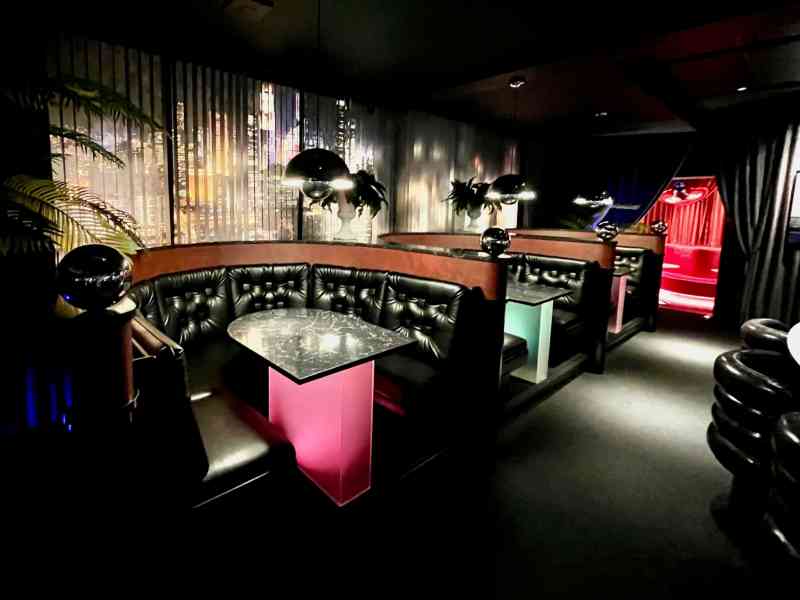 Interior view of a stylish bar with black leather booths, a glass table, and ambient lighting.