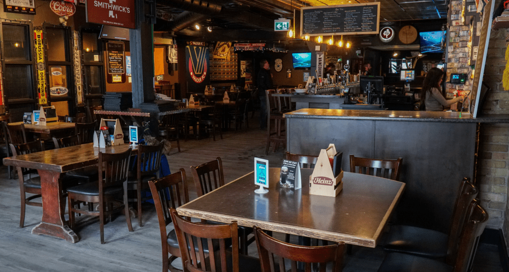 Interior view of King's Head Pub featuring wooden tables, chairs, and a bar area with various drink taps and illuminated signage.