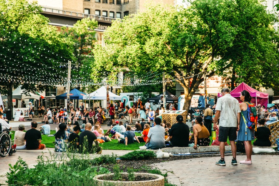 People enjoying the Winnipeg International Fringe Festival in the Exchange District, surrounded by trees, food stalls, and string lights.
