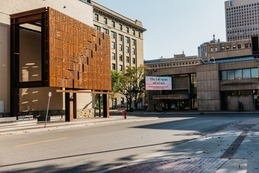 A view of the 1919 Marquee Monument in Winnipeg's Exchange District, showcasing a large, artistic structure with intricate metalwork set against historic buildings and a clear blue sky.