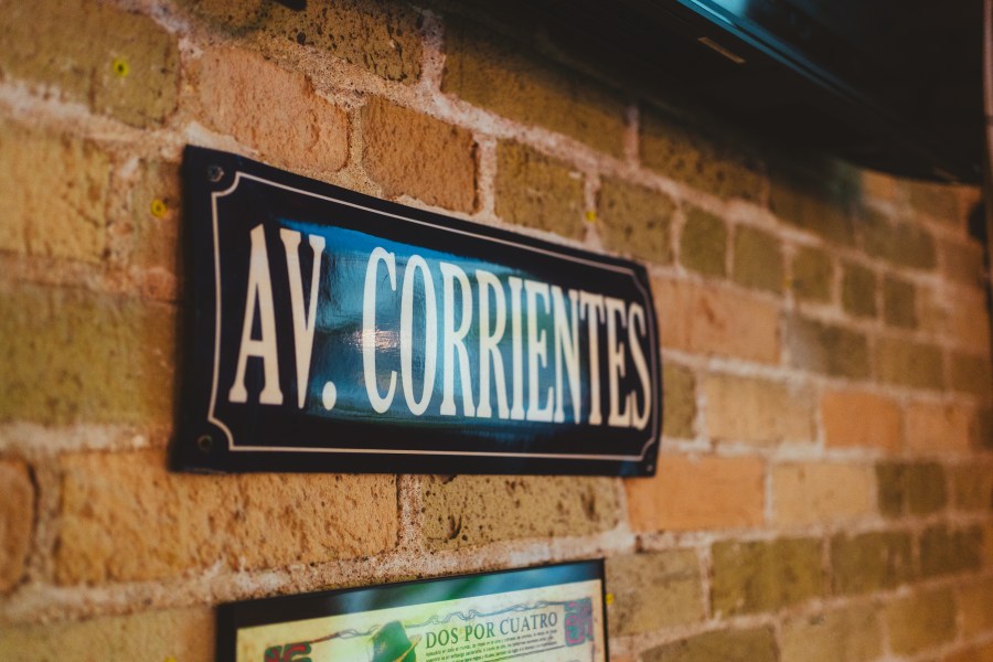 A decorative street sign featuring 'AV. CORRIENTES' mounted on a textured brick wall.